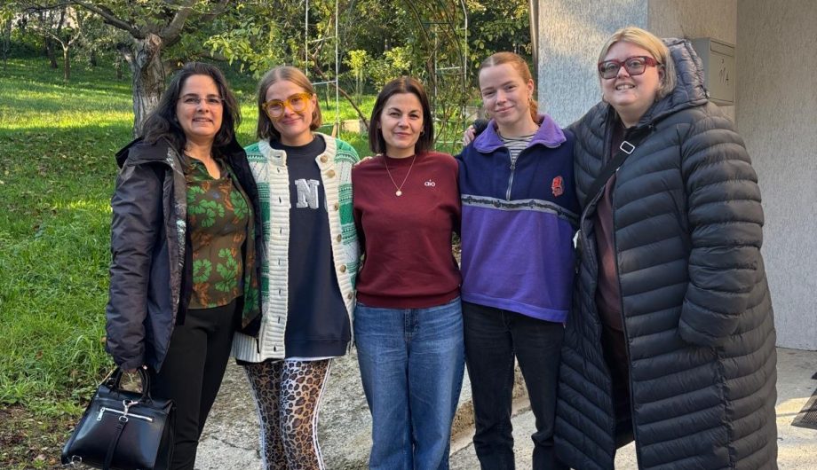 a group of five people standing next to each of smiling for the camera. There is a tree in the background