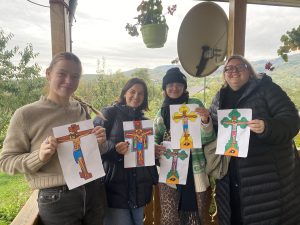 four women stand side by side holding up drawings 